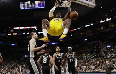 El alero de los Lakers de Los Ángeles LeBron James se cuelga del aro después de anotar en la primera mitad del juego ante los Spurs de San Antonio, el lunes 25 de noviembre de 2019, en San Antonio. (AP/Eric Gay)
